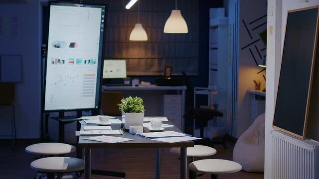 Modern empty business corporate office meeting room is ready for businesspeople late at night. In background on conference table standing company financial documents with economy graphs