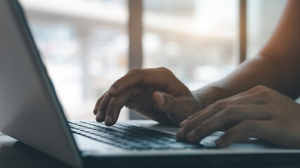 young man using laptop computer and mobile phone When looking for financial information in business, work at the desk. Writing with a pen, studying remotely from home and working from home.