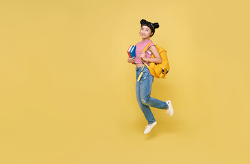 Fototapeta na wymiar Happy Asian child student jumping up with schoolbag and book isolated on yellow background.