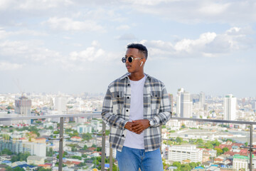 Portrait of African black man outdoors in city at rooftop during summer wearing sunglasses and...