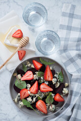 Above view of salad with beetroot, fresh strawberry and blue cheese, vertical shot on a light-grey marble background
