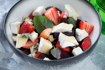 Closeup of salad with beetroot, strawberries, gorgonzola and brie cheese served in a grey bowl, selective focus
