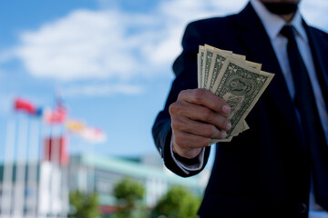 business style holding dollars and calculating. Cheerful rich handsome businessman in counting money near business center background.