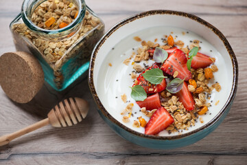 Turquoise bowl with yogurt, granola and strawberries, studio shot on a brown wooden background, selective focus