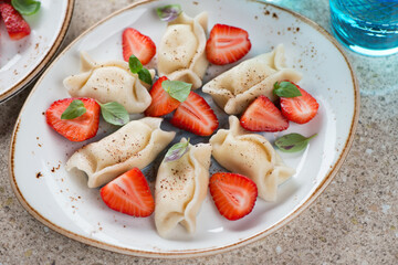 Close-up of vareniki or curd dumplings served with fresh strawberries, studio shot on a beige...