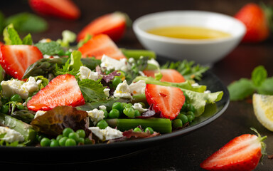 Asparagus and Strawberry Salad with vegetables, green peas and feta cheese in black plate. healthy food.