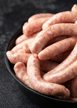 Raw pork chipolata sausage in cast iron skillet frying pan