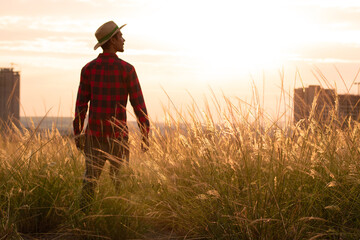 Farmer with hat in farm plantation on sunset. Buildings and city blurred background. Space for text.