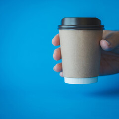 Close up of Man Hand Holding a Recycle Brown Paper Coffee Cup on a Blue Background, Mockup Template for Logo Design, Branding, Copy Space for Text.