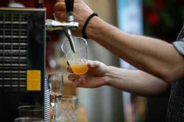 Shallow depth of field (selective focus) image with a man pouring craft beer from a dispenser into a plastic glass.