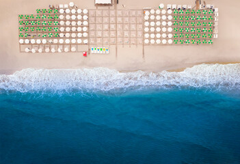 Top view of the beach and sunbeds by the blue sea. Beautiful seascape, water and sand. Vacation by the ocean.