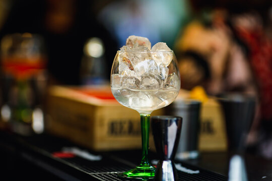 Shallow depth of field (selective focus) image with a glass with ice cubes and vodka on the counter of a bar.
