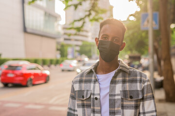 Portrait of African black man outdoors in city during summer wearing face mask back lit shot with lens flare