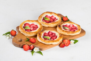 Small open pies made of puff pastry with cottage cheese and fresh strawberries on a wooden board on a white background