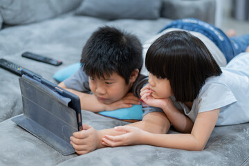 two chinese children addicted tablet, asian child watching telephone together on their bed, kid using smartphone