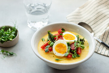 polenta bowl with fresh vegetables, microgreens and eggs on gray table. Healthy food concept. blurred background