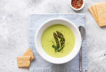 Vegan asparagus soup in bowl on linen napkin and rice crackers. Tasty vegan food, plant based diet concept. flat lay
