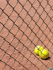 Pair of yellow softballs in dirt behind chain link fence