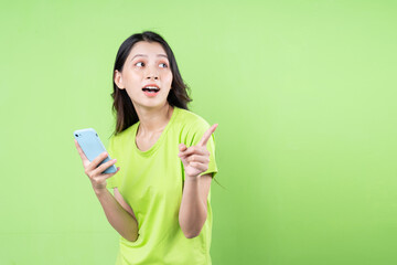 Image of young asian woman holding smartphone on green background