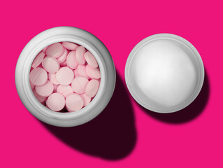 top view of pink pills in white bottle and cap on magenta background