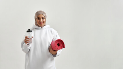 Smiling young arabic woman in hijab holding sport mat