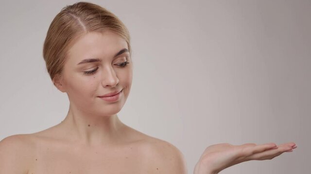 Close up beautiful young caucasian blonde woman with grey eyes and smooth healthy skin holding a hand. White Cream Skin Care Cosmetic Concept. Slow Motion On grey background.
