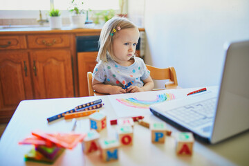Unhappy and tired toddler girl in front of laptop