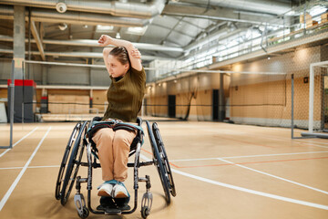 Full length portrait of young woman in wheelchair warming up before sports practice at volleyball court, copy space