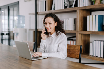 Fototapeta premium Young businesswoman talking on the phone with happy customers on her home desk, work from home concept