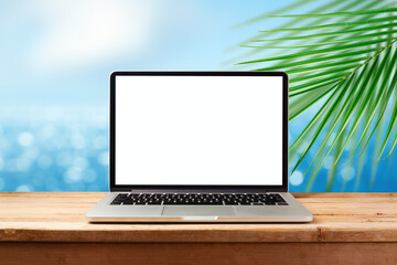 Laptop computer with blank screen on wooden table over sunny tropical beach background. Summer vacation mock up for design