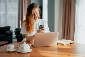 A female blogger types text on a laptop. The housewife keeps a record of expenses in the table online. Student beautiful girl study at home remotely.