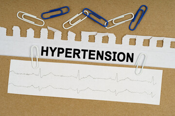 On the table lies a cardiogram, paper clips and paper with the inscription - HYPERTENSION