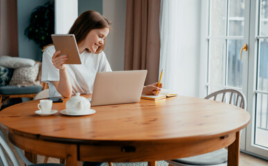 A female blogger types text on a laptop. The housewife keeps a record of expenses in the table online at home. Student beautiful girl study at home remotely.