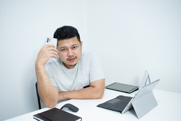 Portrait of a nice smiling grey hair man with beard, working at home on some project, he is sitting at a white table looking at camera, writing ideas with his laptop in front of him. Focus on the man