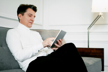 A teacher in a comfortable suit is looking at the computer. Sitting on a comfortable couch, typing out a progress report on a new startup. Portrait of an adult creative person.