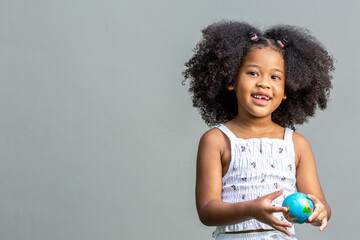 Child, woman, afro hairstyle holding a mock globe in hand showing emotions and poses. Isolated on gray background, childhood, and emotion concept.