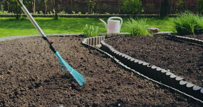 Farmer working in garden, loosening soil with rake for planting. Landscaping, farming, gardening concept
