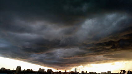 A black and blue thundercloud creeping over the city from the horizon. Atmospheric urban landscape. Stylish wallpaper or a print with a creative take on a natural phenomenon.