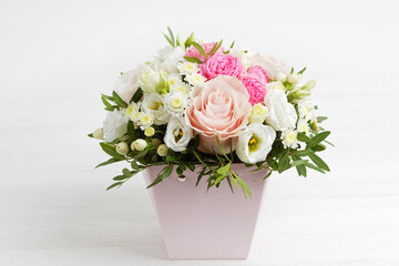 Bouquet of different flowers in a pink pot on white wooden table.