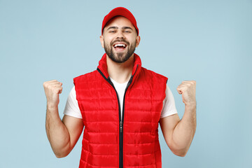 Naklejka premium Professional delivery guy employee man in red cap white T-shirt vest uniform workwear work as dealer courier winner celebrate isolated on pastel blue color background studio portrait. Service concept.