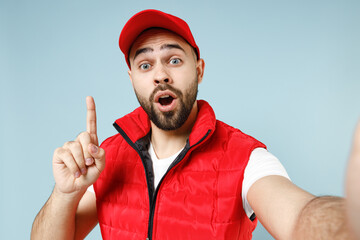 Close up professional delivery guy employee man in red cap white T-shirt uniform workwear work as dealer courier doing selfie isolated on pastel blue color background studio portrait. Service concept.