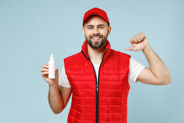 Delivery guy employee man in red cap white T-shirt vest uniform workwear work dealer courier hold bottle spray sanitizer soap isolated on pastel blue color background studio portrait. Service concept.