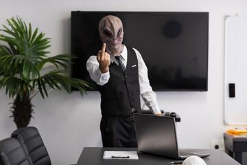 Man wearing a mask of an alien looking at camera and showing middle finger in the office....