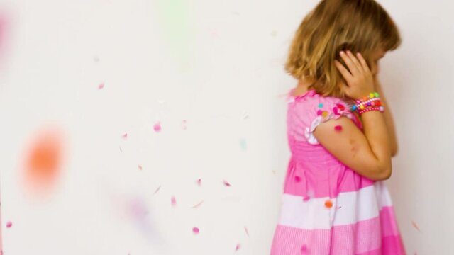 Slow motion of a cute little girl throwing confetti over her head and spinning while confetti falling over her head