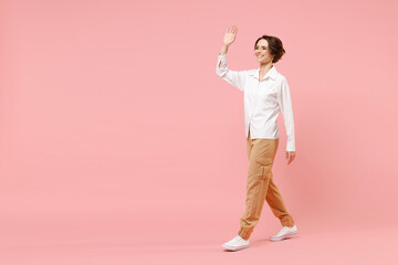 Fototapeta na wymiar Full length side view fun young smiling successful employee business woman corporate lawyer in classic formal white shirt work in office walking waving hand isolated on pastel pink background studio.