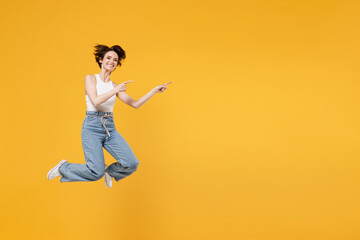 Full length young fun happy amazed woman 20s with bob haircut wearing white tank top shirt jumping high pointing index finger aside on copy space area mock up workspace isolated on yellow background.