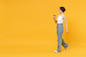 Fototapeta na wymiar Full length side view young happy woman 20s with bob haircut in white tank top shirt hold takeaway delivery craft paper brown cup coffee to go walk isolated on yellow color background studio portrait.