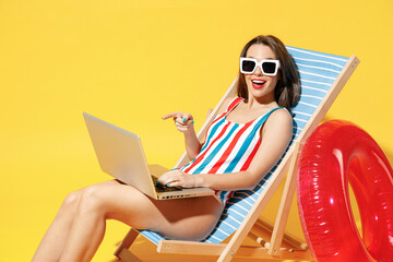 Full body length happy young woman wear red blue one-piece swimsuit sit on chair work hold laptop...