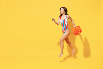 Fototapeta na wymiar Full length fun happy sexy woman slim body wear red blue one-piece swimsuit jump high air run fly hold lifebuoy isolated on vivid yellow color background studio Summer hotel pool sea rest sun concept