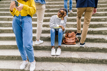 Portrait of unhappy and sad african female student sitting on the stairs, outdoor while indifferent...